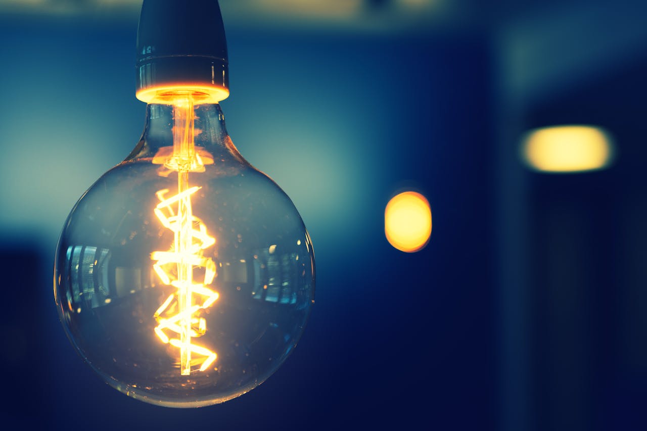 Accueil A close-up image of a glowing lightbulb with a warm tone against a blurred background.