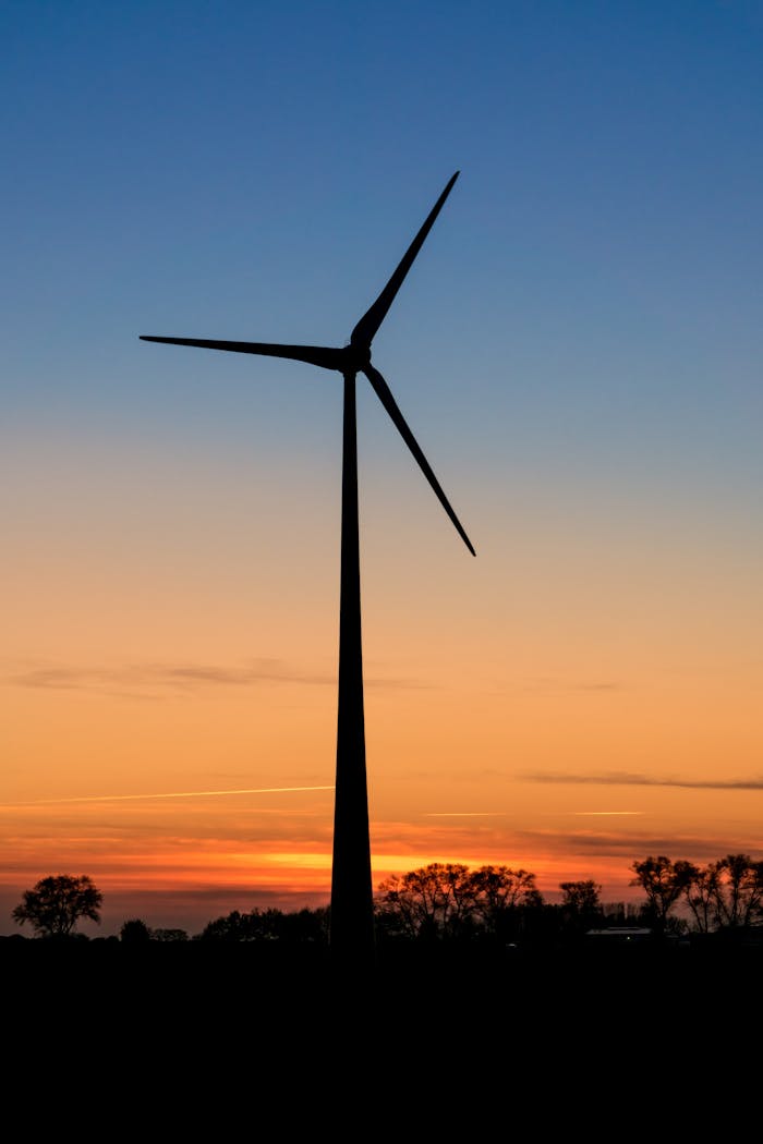 Accueil A lone wind turbine silhouetted against a vibrant sunset sky, symbolizing renewable energy.