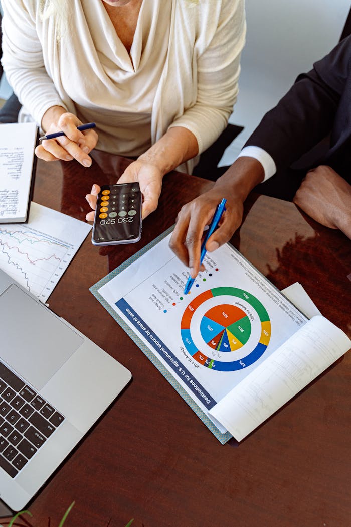Accueil Two business professionals discussing financial documents and strategies at an office desk.