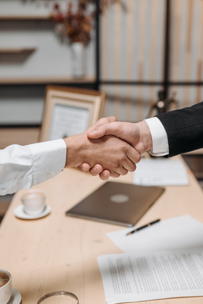 Accueil Close-up of two people shaking hands in an office, symbolizing agreement and partnership.